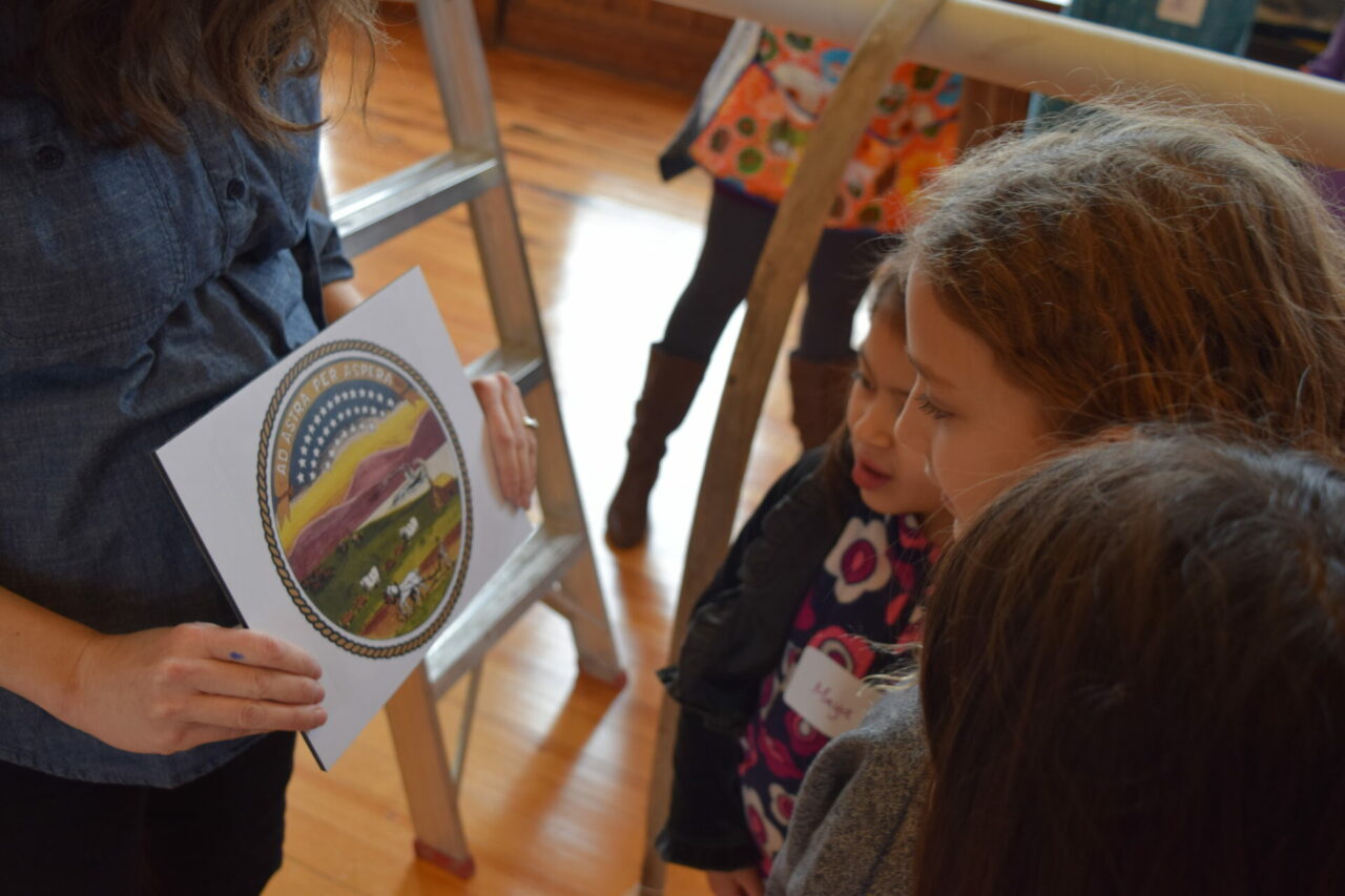 Three children look at the seal of Kansas